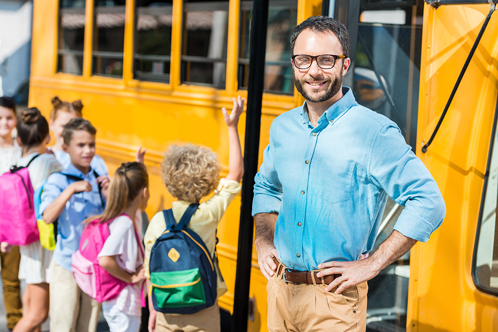 school bus driver standing in front of school bus with a line of children