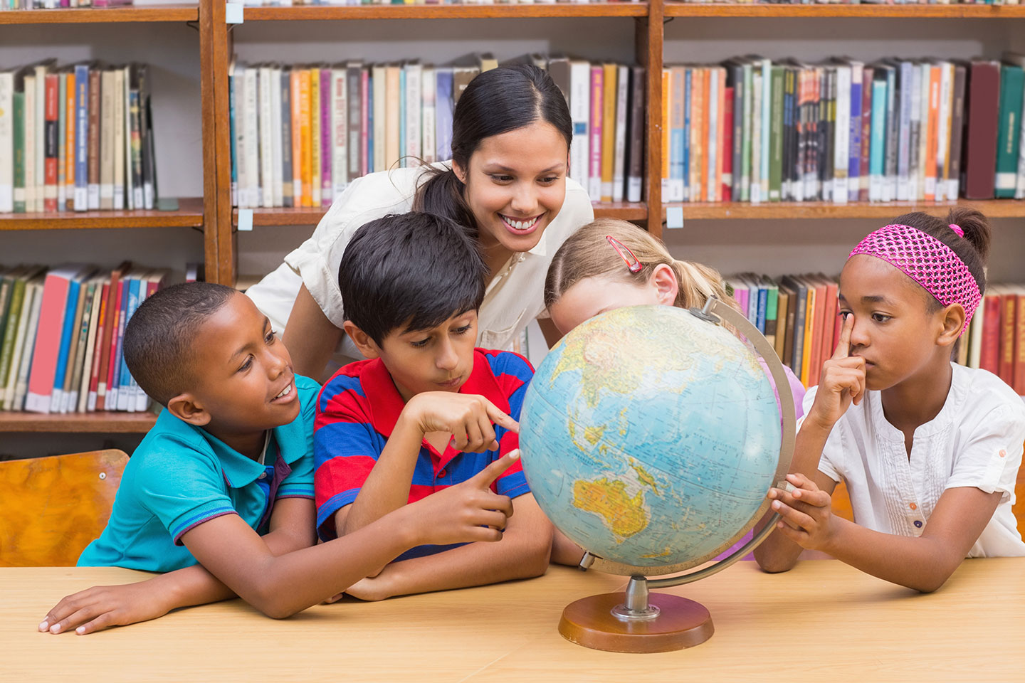 teacher with a group of students pointing at a globe